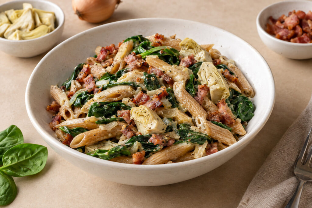 Penne met spinazie artisjok en hummus met spekblokjes in een kom