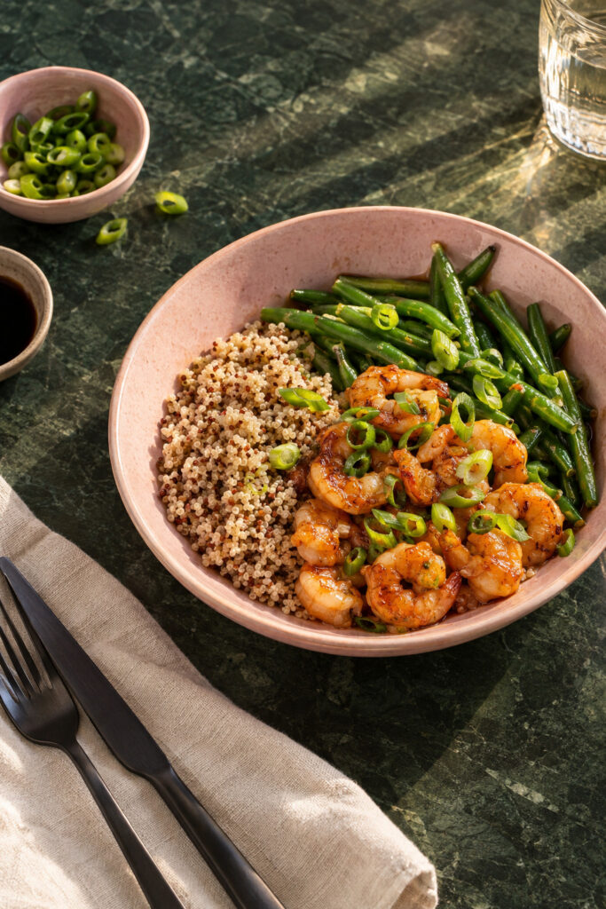 Quinoa met teriyaki garnalen en sperziebonen met bosui op een bord